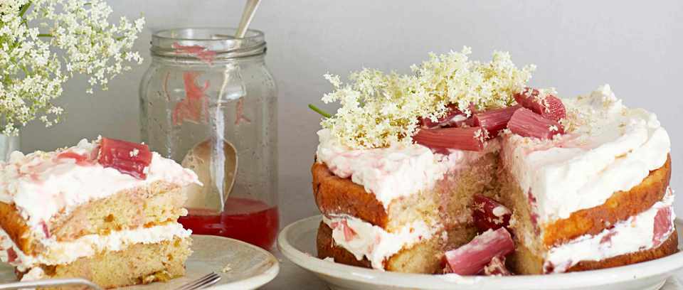 Elderflower & rhubarb cake on a white plate next to a jar of jam