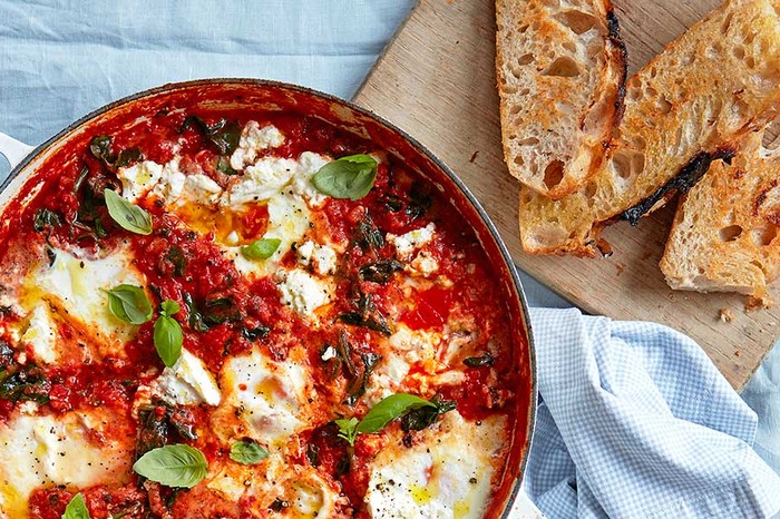 Baked eggs in a casserole dish with spinach, tomatoes, ricotta & basil