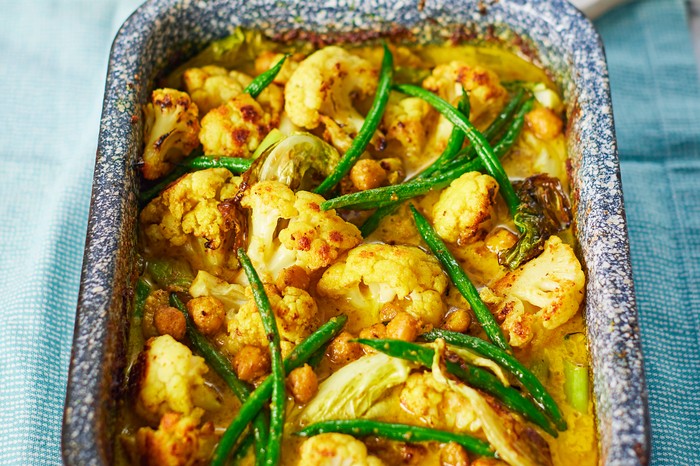 Oven dish filled with cauliflower, green beans and chickpeas covered in spices