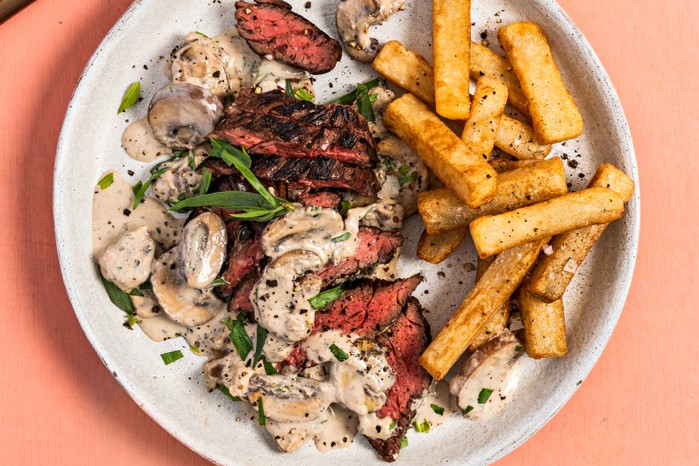 Bavette steak served rare in slices on a plate with chips and a creamy sauce