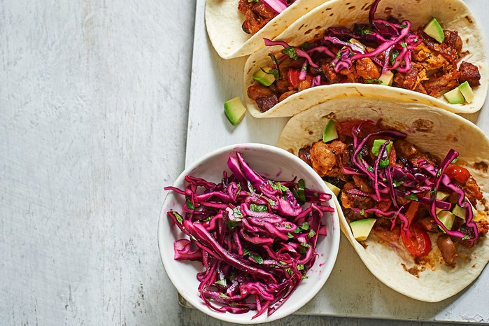 Chorizo tacos topped with red cabbage slaw, next to a bowl of the red cabbage slaw