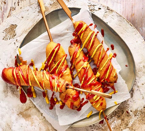 Corndogs on a plate topped with ketchup and mustard