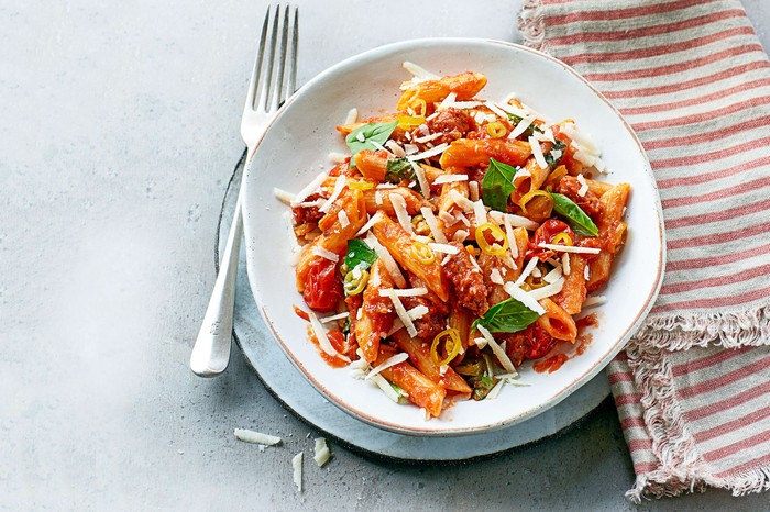 A white bowl of chorizo pasta with a napkin on the side