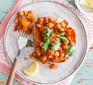 Vegan chickpea curry jacket potato on a plate with a slice of lemon and fork alongside