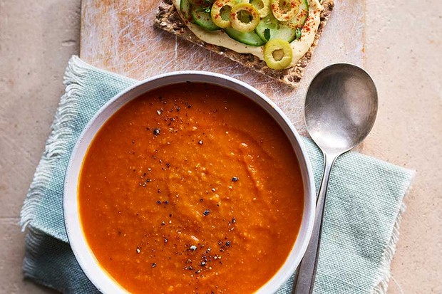 A serving of tomato soup in a bowl with a hummus crispbread